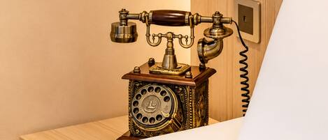 A vintage telephone on a wooden table in a room with a wooden wall and a white bed.