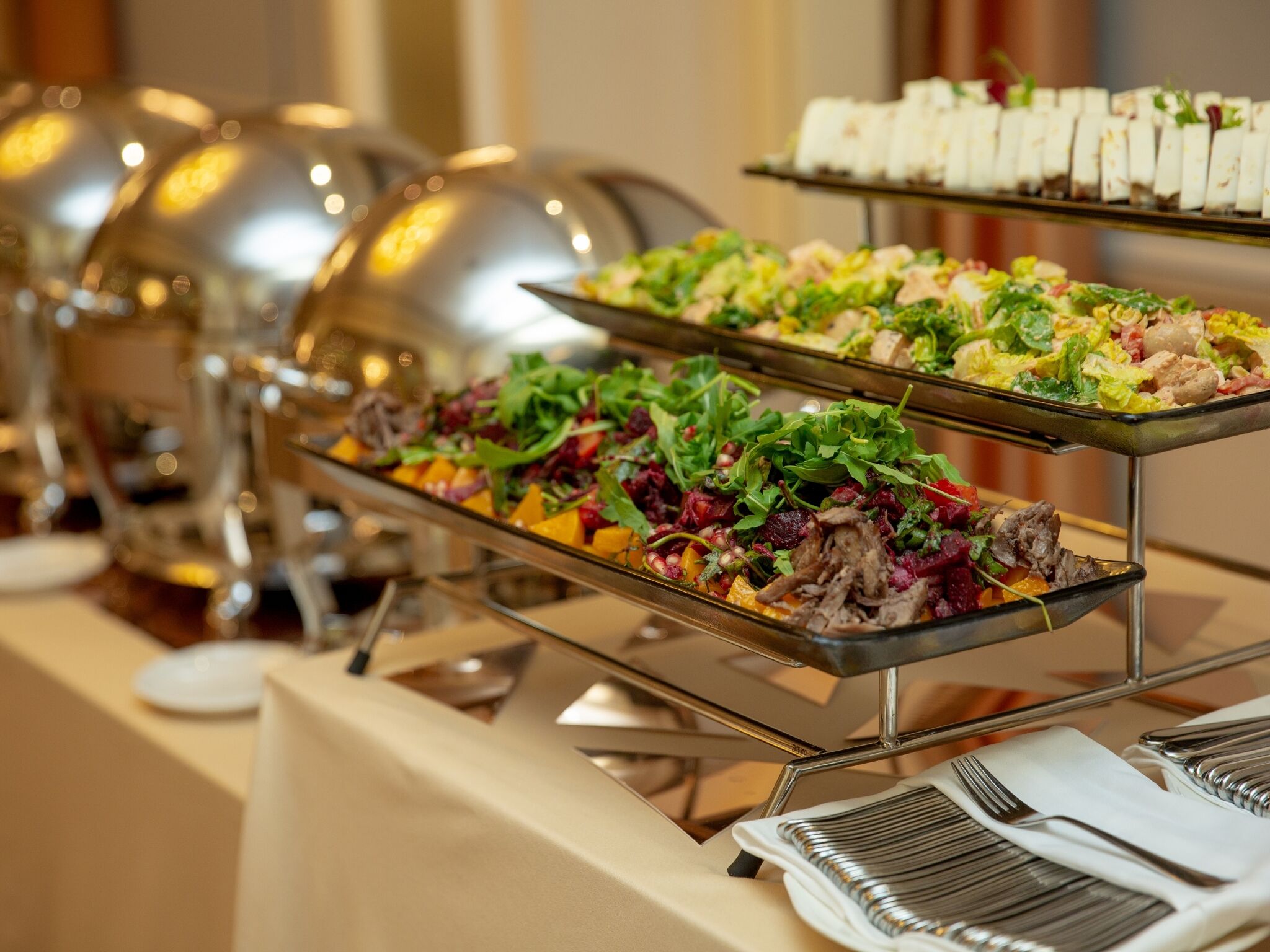 Un buffet con diversi piatti, tra cui insalate e carni, disposti su supporti metallici.