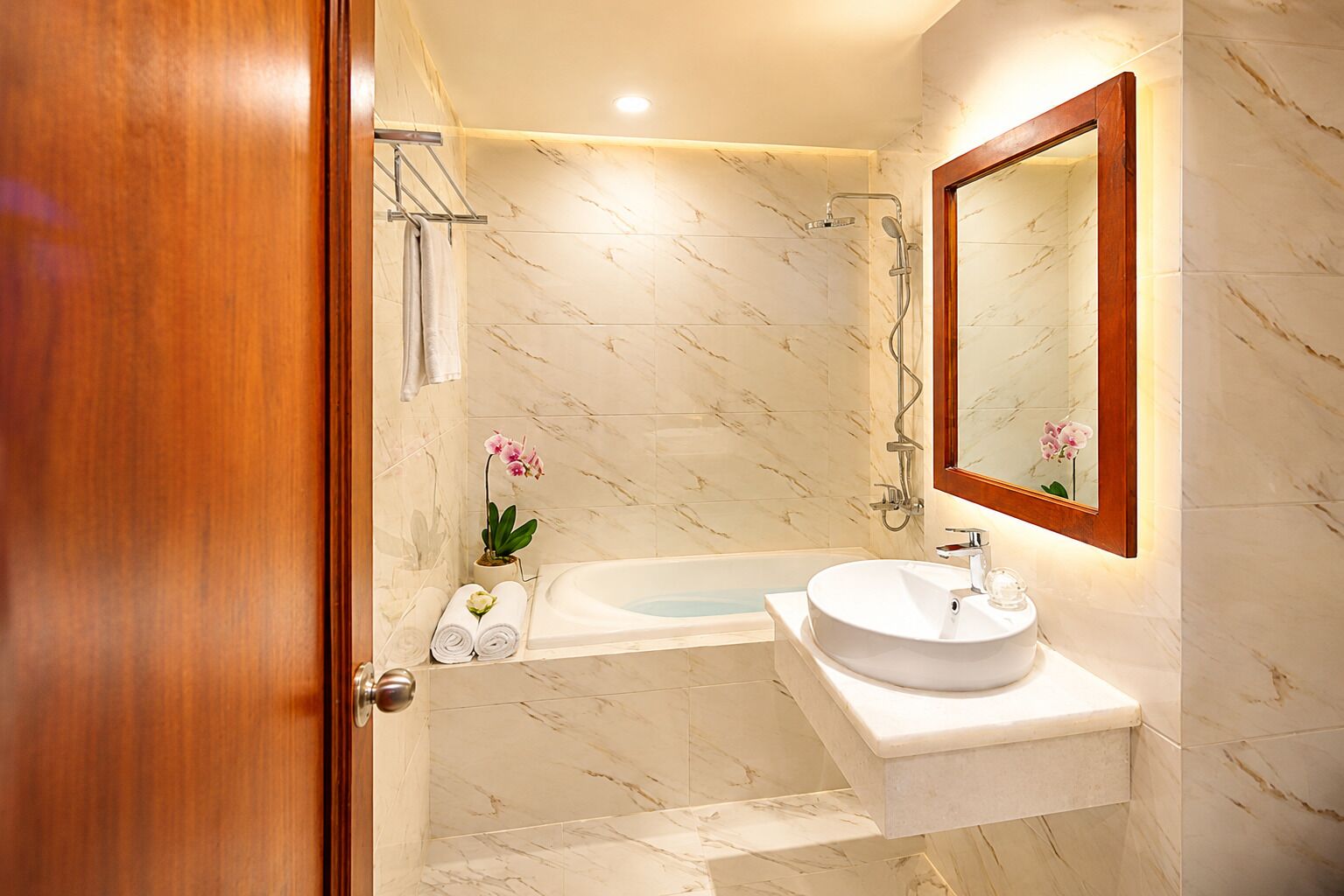 Un baño con pared de mármol, una bañera, un lavamanos y un espejo.