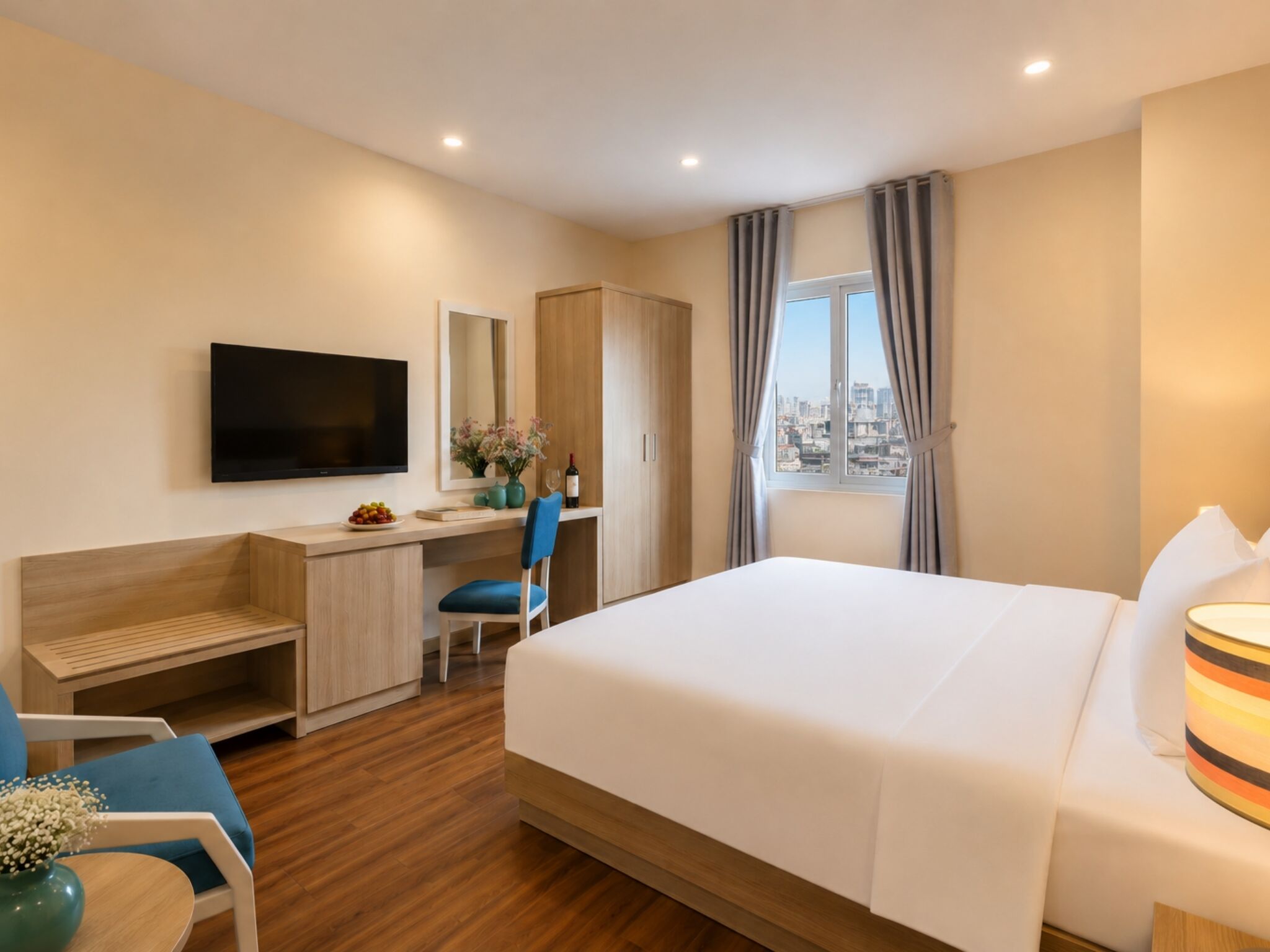 Quarto de hotel com cama, escrivaninha, cadeira, televisão e janela com cortinas.