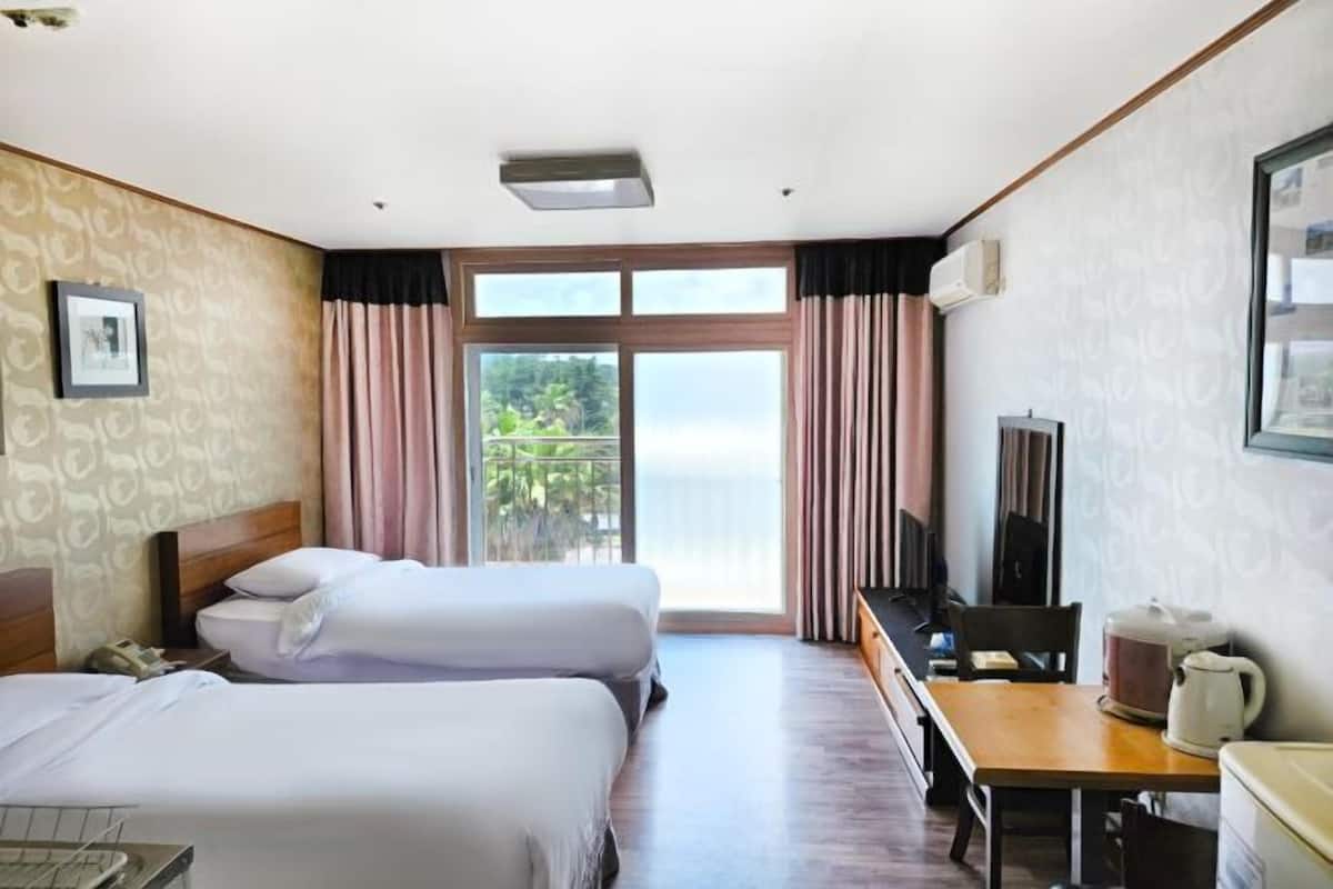 Une chambre d’hôtel avec deux lits, un bureau, une chaise, une télévision et un balcon avec des rideaux.