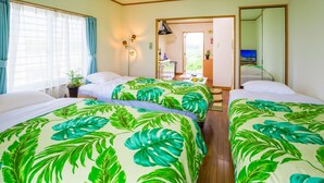 Habitación de hotel con tres camas, cada una con una colcha de estampado de hojas tropicales. Se ve una ventana con cortinas azules, una puerta que da a un balcón y una pequeña mesa con una planta y una botella.