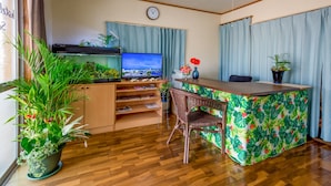 Un espacio habitable compacto con piso de madera, kitchenette, comedor con silla de mimbre, televisor y un reloj en la pared.