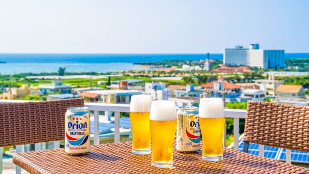 Una mesa con cuatro vasos de cerveza y una lata sobre una silla de mimbre con vista a una ciudad costera.