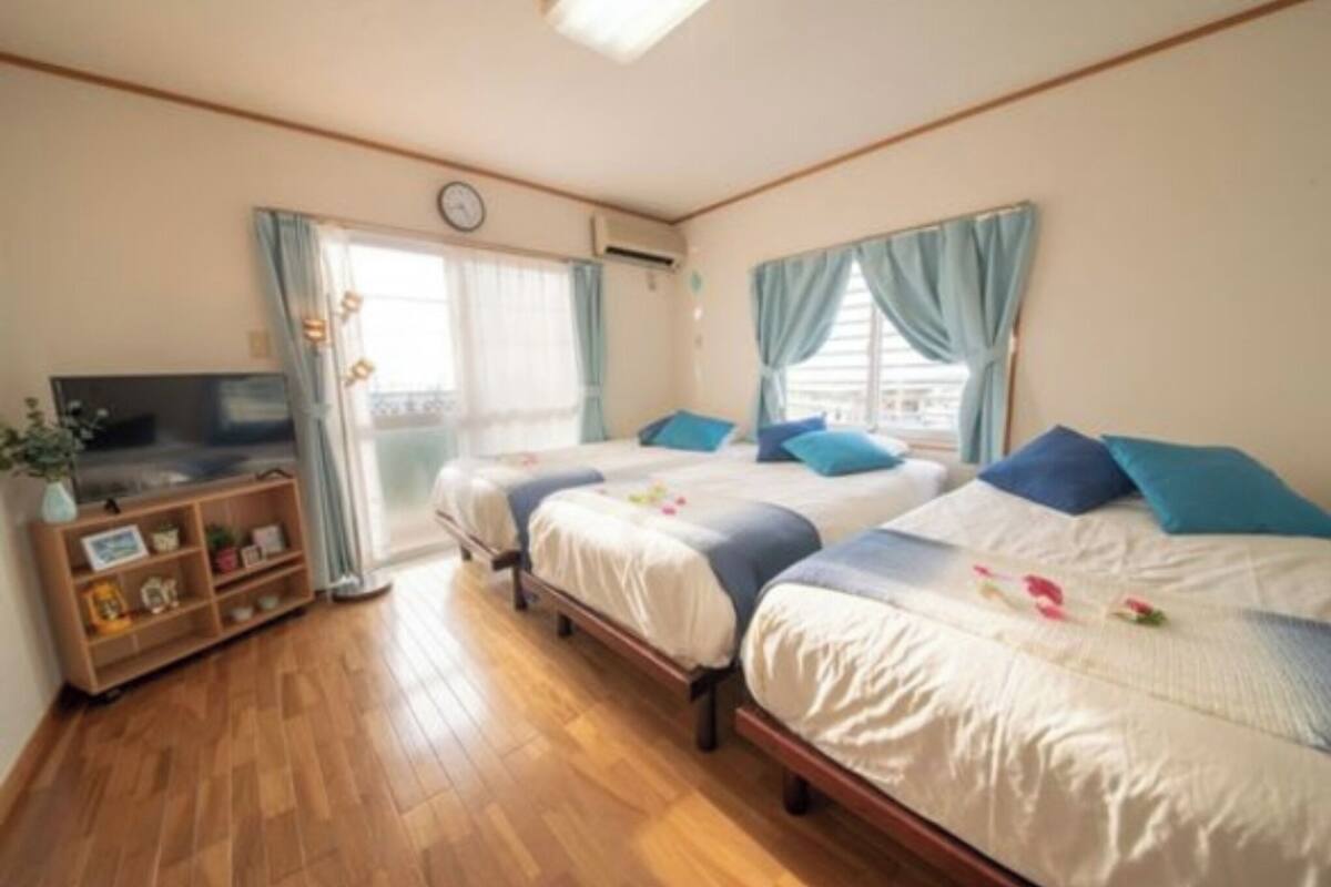 Ein Hotelzimmer mit zwei Betten, einem Fernseher, einem Holzregal und einem Fenster mit Vorhängen.