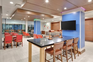 A modern dining area with a long table, red chairs, and a blue accent wall.