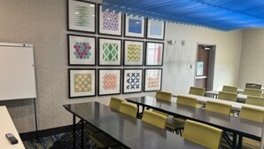 Een vergaderruimte met een lange tafel, gele stoelen en lijstjes met patronen aan de muur.