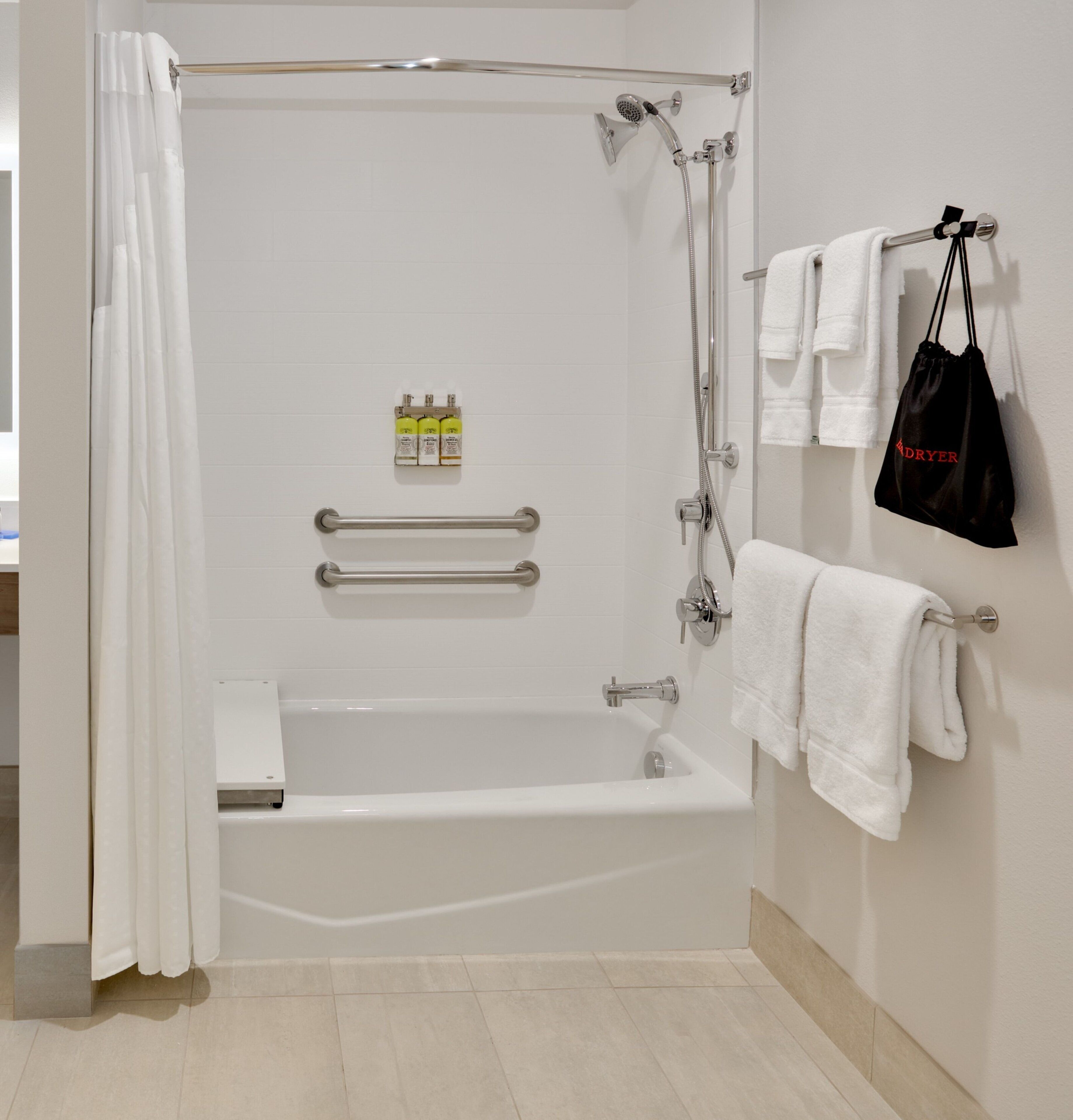Un baño con bañera, ducha, tendedero para toallas y una bolsa colgada en la pared.