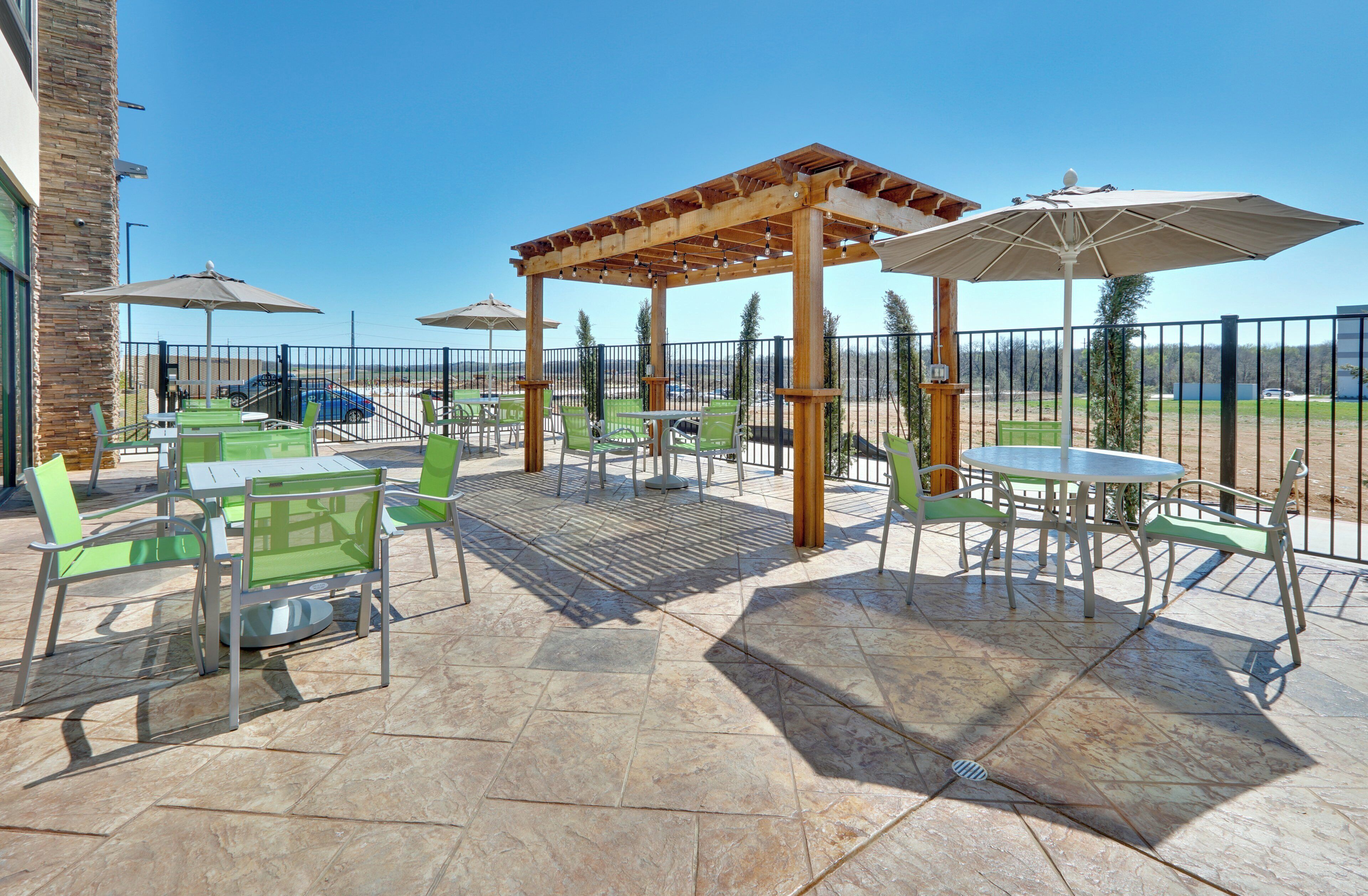 Un patio al aire libre con mesas y sillas, una pérgola y vistas del paisaje circundante.