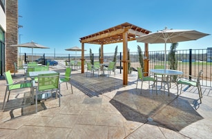 Un patio al aire libre con mesas y sillas, una pérgola y vistas del paisaje circundante.