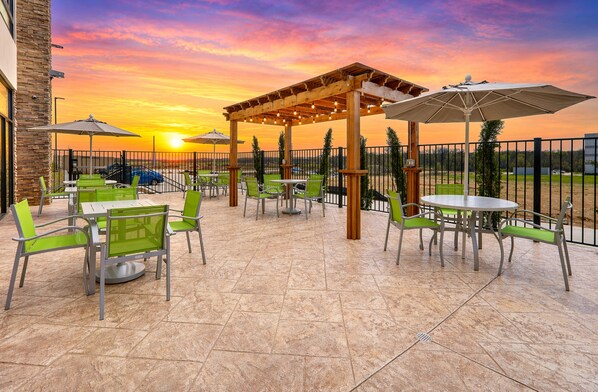 An outdoor patio with tables and chairs, a pergola, and a sunset view.