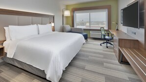 Een hotelkamer met een groot bed, een bureau met stoel, een televisie en een raam met uitzicht op de stad.