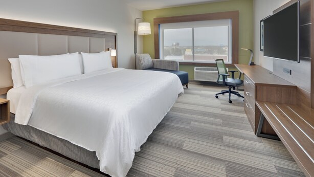 Een hotelkamer met een groot bed, een bureau met stoel, een televisie en een raam met uitzicht op de stad.