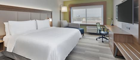 Habitación de hotel con una cama grande, un escritorio con silla, televisor y ventana con vistas.