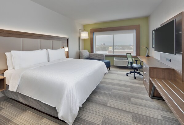Une chambre d’hôtel avec un grand lit, un bureau avec une chaise, une télévision et une fenêtre donnant sur la ville.