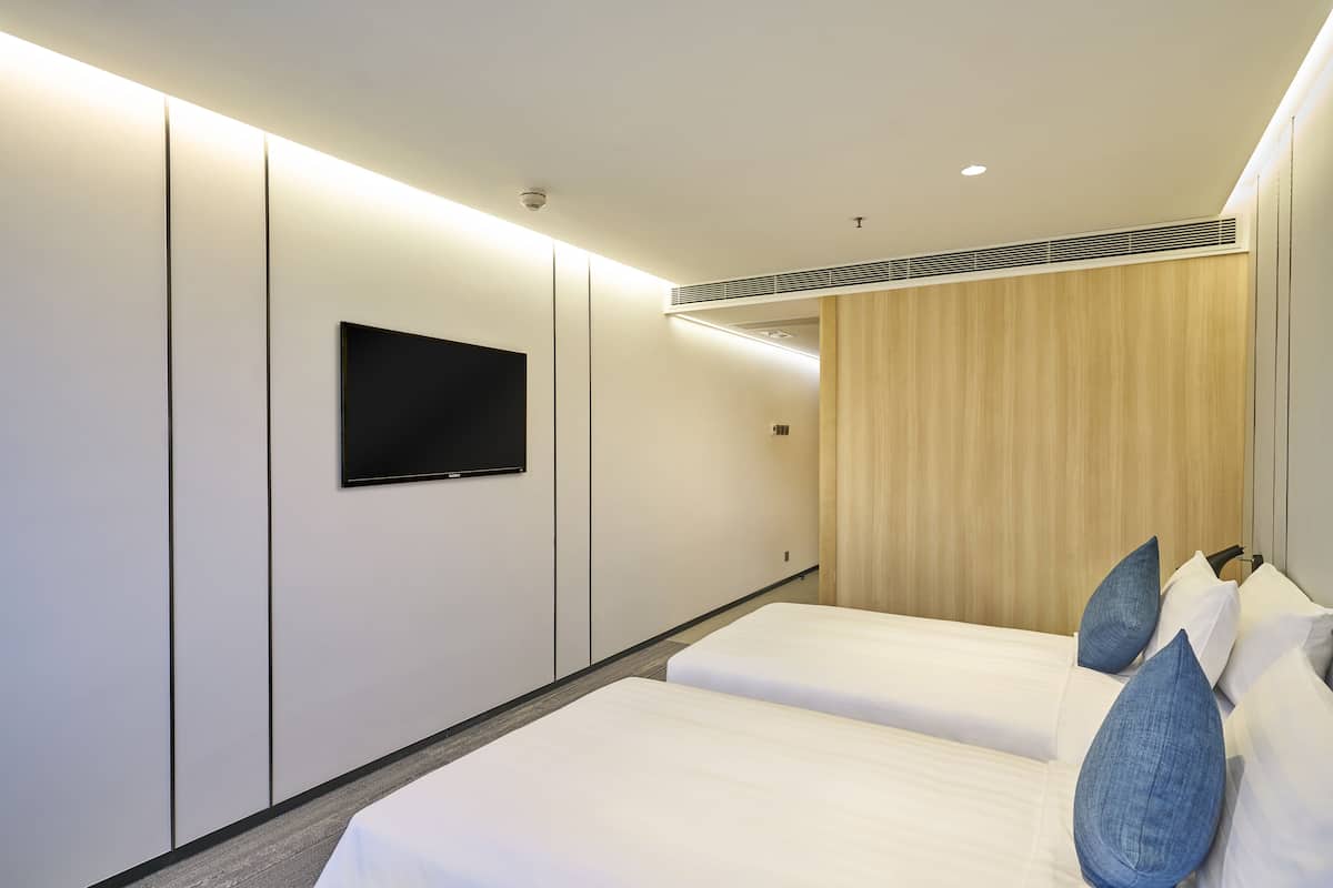 A modern hotel room with two beds, a flat-screen TV mounted on the wall, and a wooden panel wall.