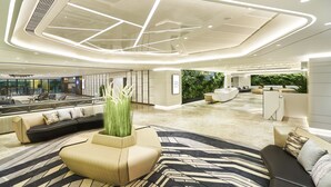 A spacious lobby with a modern design, featuring a large seating area, a reception desk, and a view of the outdoors. - Hotel COZi · Oasis (Kwai Chung)