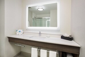 Un baño con un lavamanos blanco, un espejo y un perchero para toallas.