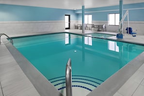 A swimming pool with clear blue water, tiled walls, and a sunlit room with a door and a window. - Holiday Inn Express - Village West (Kansas City)