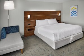 A hotel room with a large bed, a bedside table with a lamp, a chair, and a wall-mounted artwork. - Holiday Inn Express - Village West (Kansas City)