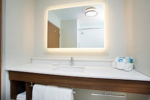 Un baño con lavamanos blanco, espejo y tocador de madera.