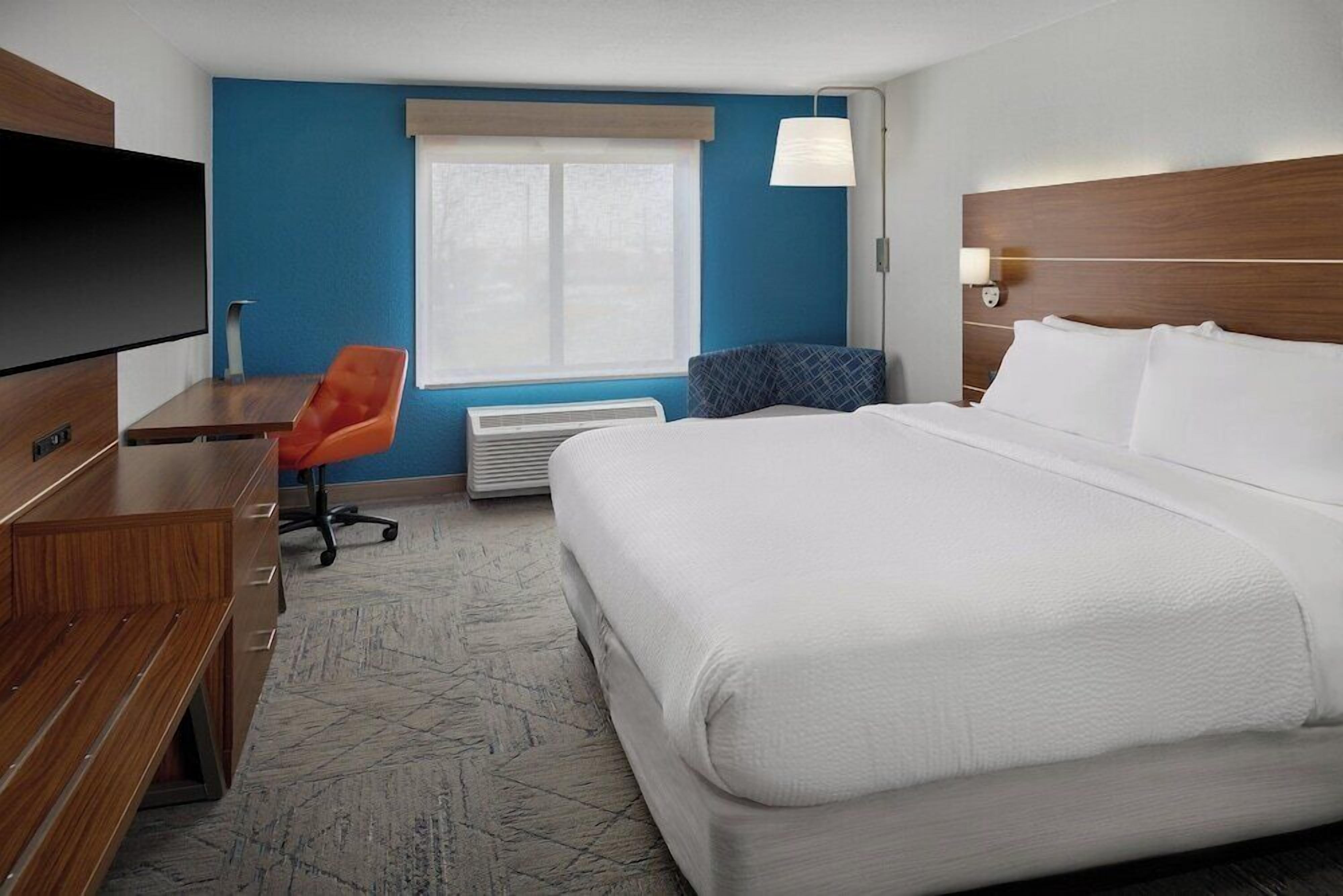 A hotel room with a bed, a desk, a TV, and a window.