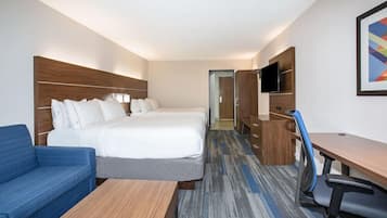 A hotel room with a large bed, a desk, a chair, a sofa, and a TV mounted on the wall.