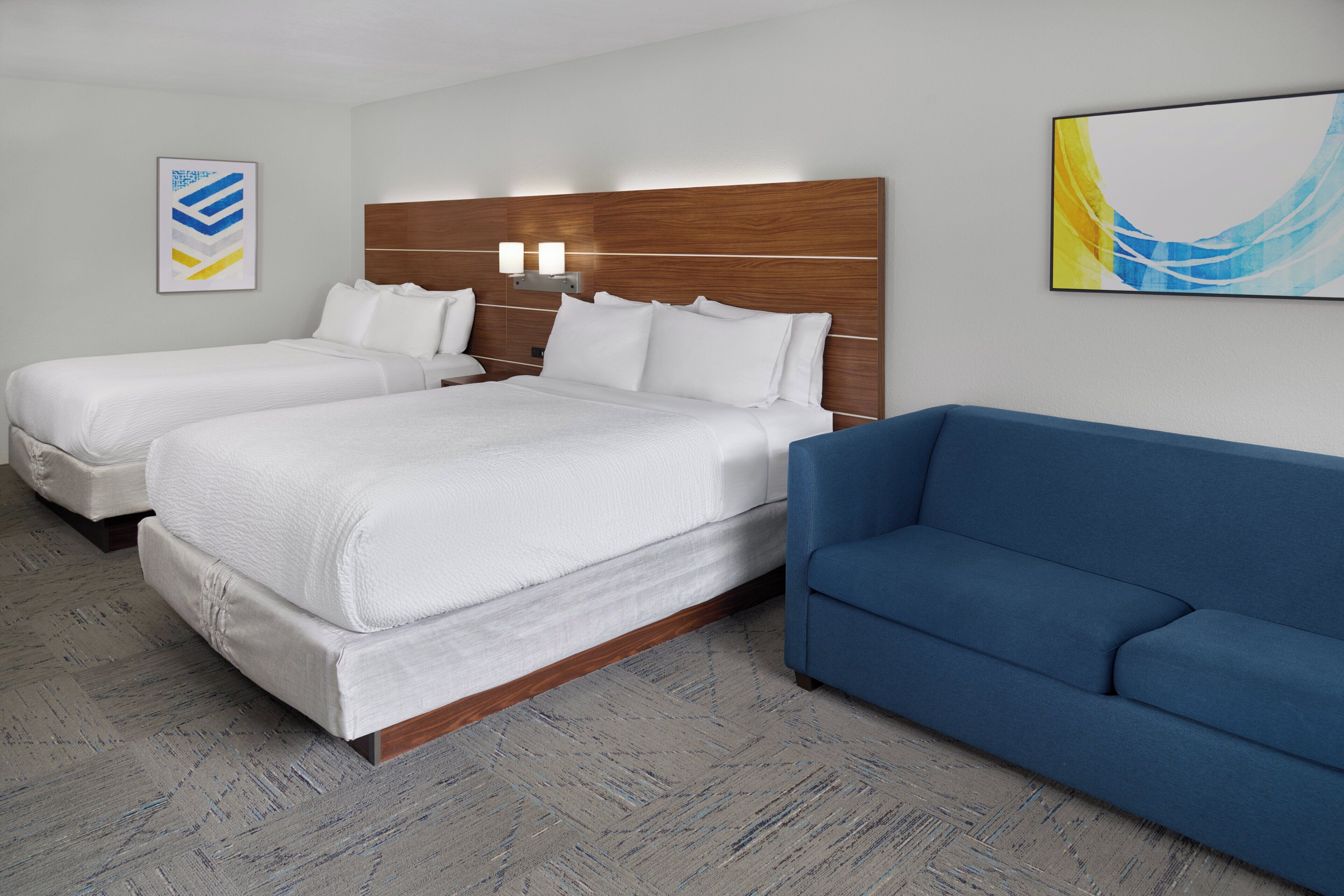 A hotel room with two beds, a blue sofa, and a wooden headboard.