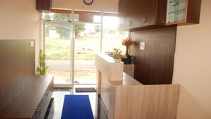 A reception area with a wooden counter, a clock, and a view of the outdoors. - Kings Inn (Bengaluru)