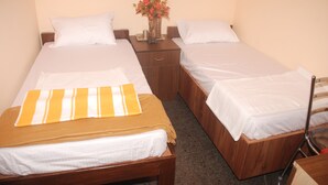 A hotel room with two single beds, a wooden nightstand with a vase of flowers, and a chair. - Kings Inn (Bengaluru)
