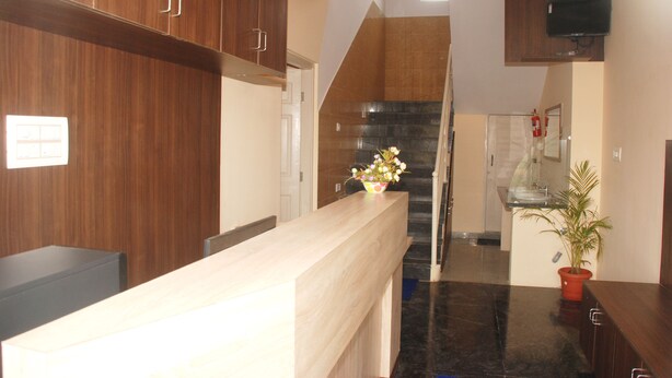 A reception area with a wooden reception desk, a potted plant, and a staircase leading to an upper floor. - Kings Inn (Bengaluru)
