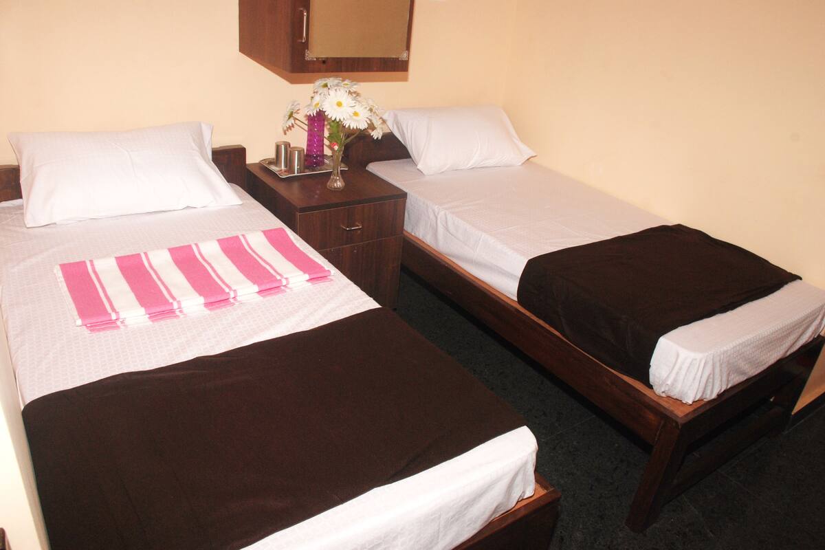 A hotel room with two single beds, a nightstand with a vase of flowers, and a wooden headboard.