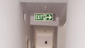 A corridor with an exit sign, a window, and a fire extinguisher. - Kings Inn (Bengaluru)