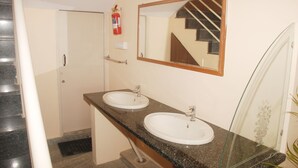 A bathroom with two sinks, a mirror, and a fire extinguisher. - Kings Inn (Bengaluru)