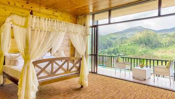 A room with a bed, a balcony with outdoor furniture, and a view of a green landscape.