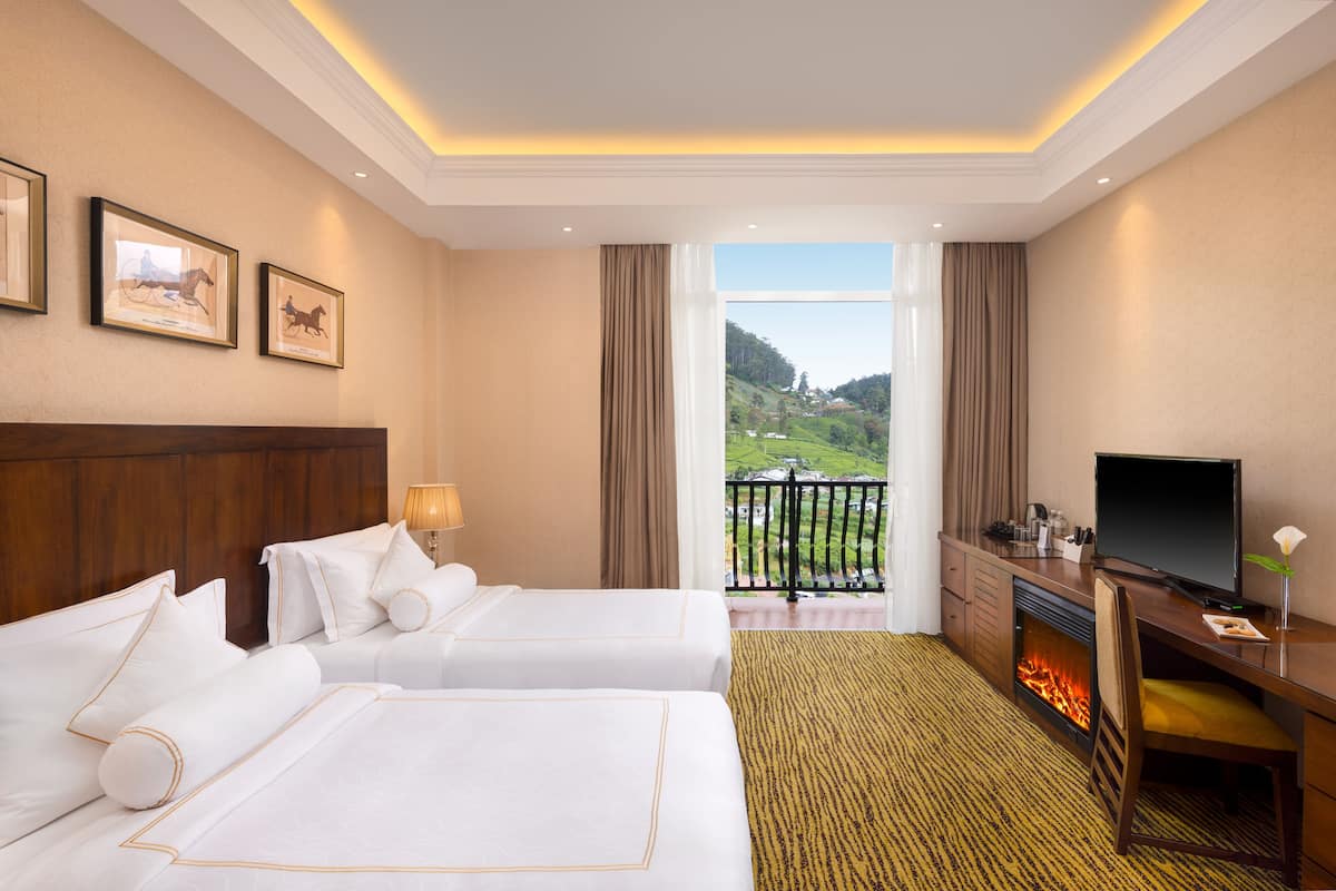 A hotel room with two beds, a desk with a TV, a fireplace, and a balcony with a view of the countryside.
