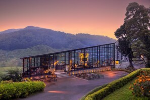 A modern glass building with outdoor seating and a view of a mountainous landscape. - The Golden Ridge Hotel (Nuwara Eliya)