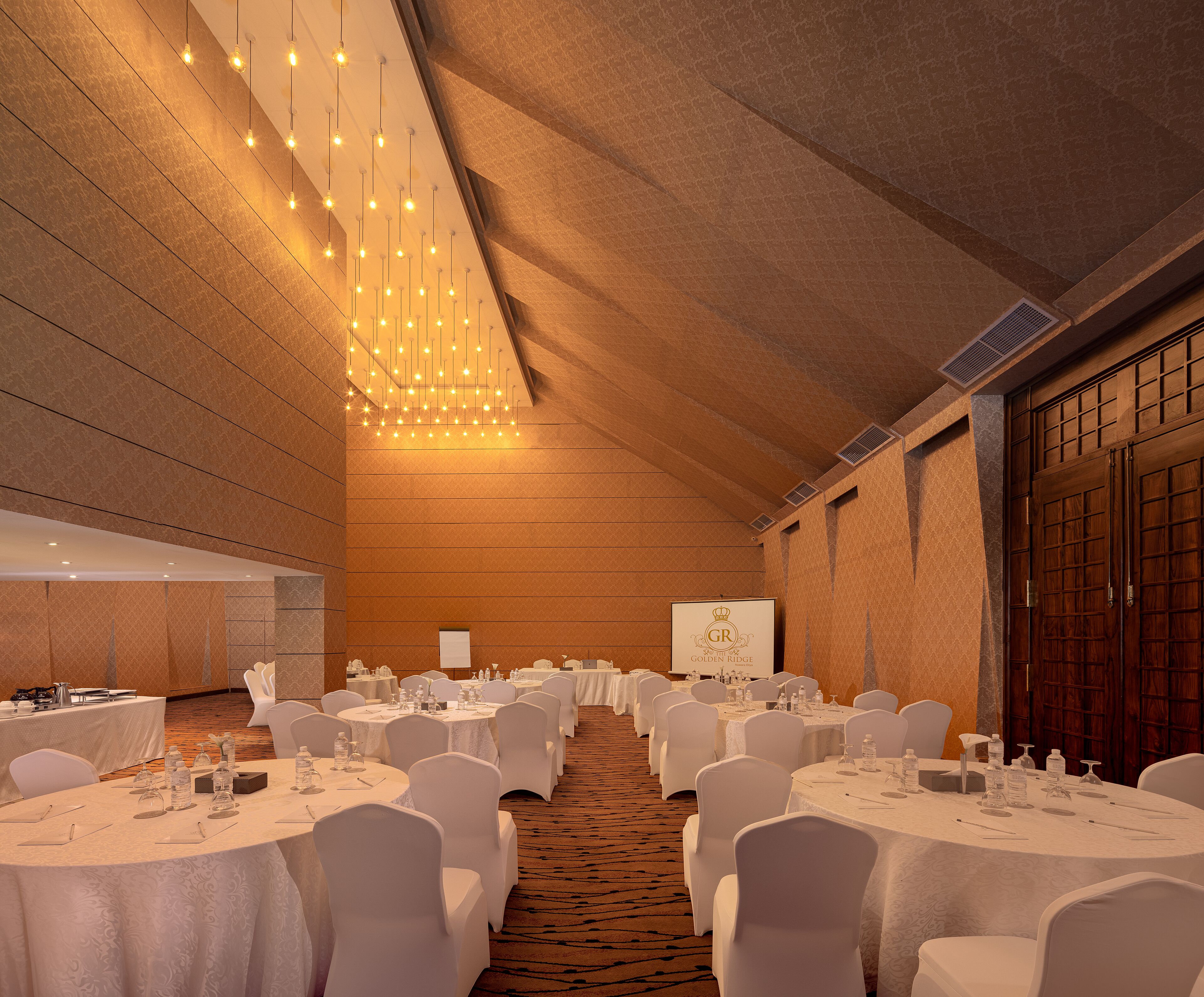 A banquet hall with round tables, white chairs, and a carpeted floor.