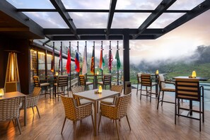 A restaurant with outdoor seating, flags, and a view of the landscape. - The Golden Ridge Hotel (Nuwara Eliya)