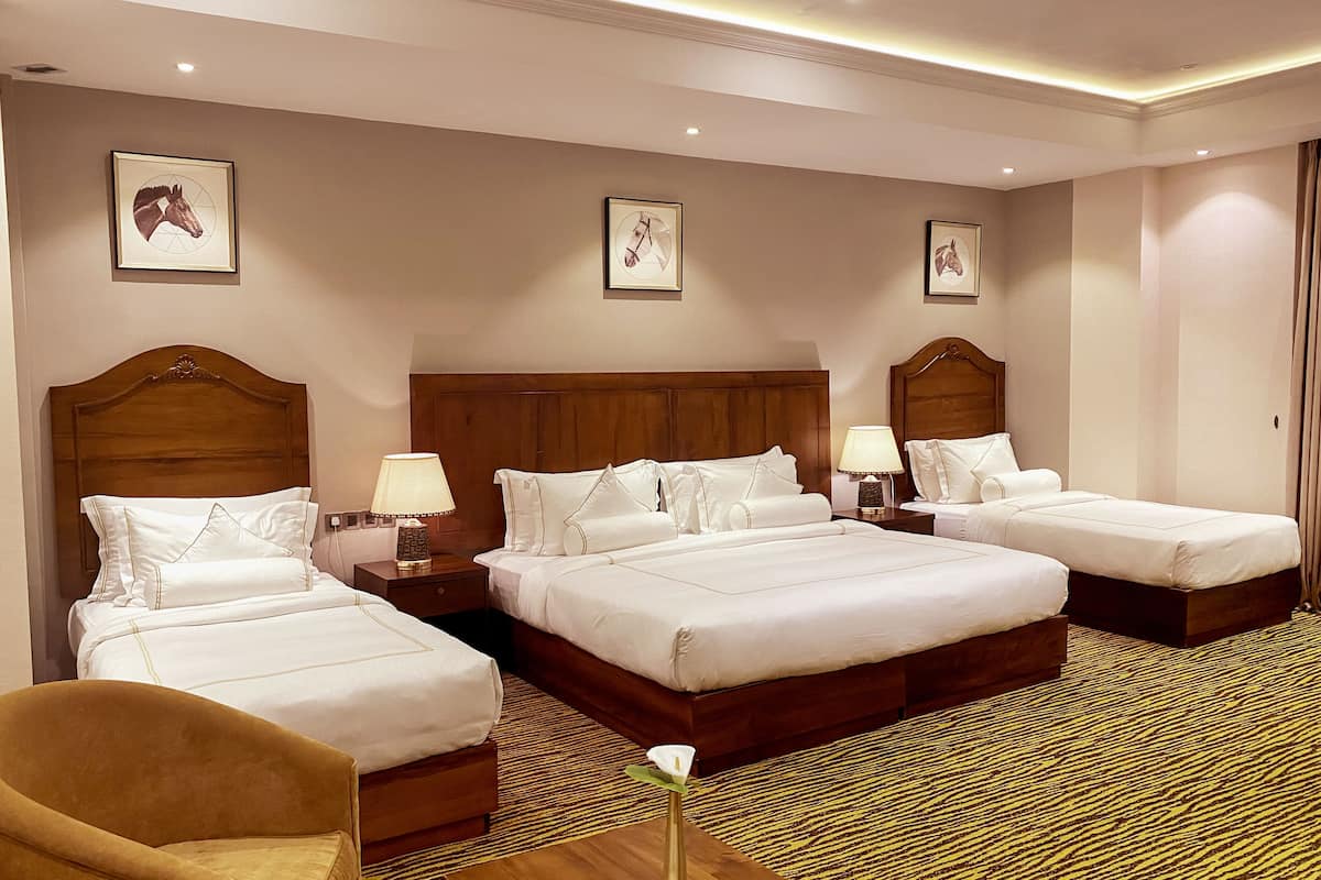 A hotel room with three beds, a wooden headboard, white bedding, and a patterned carpet.