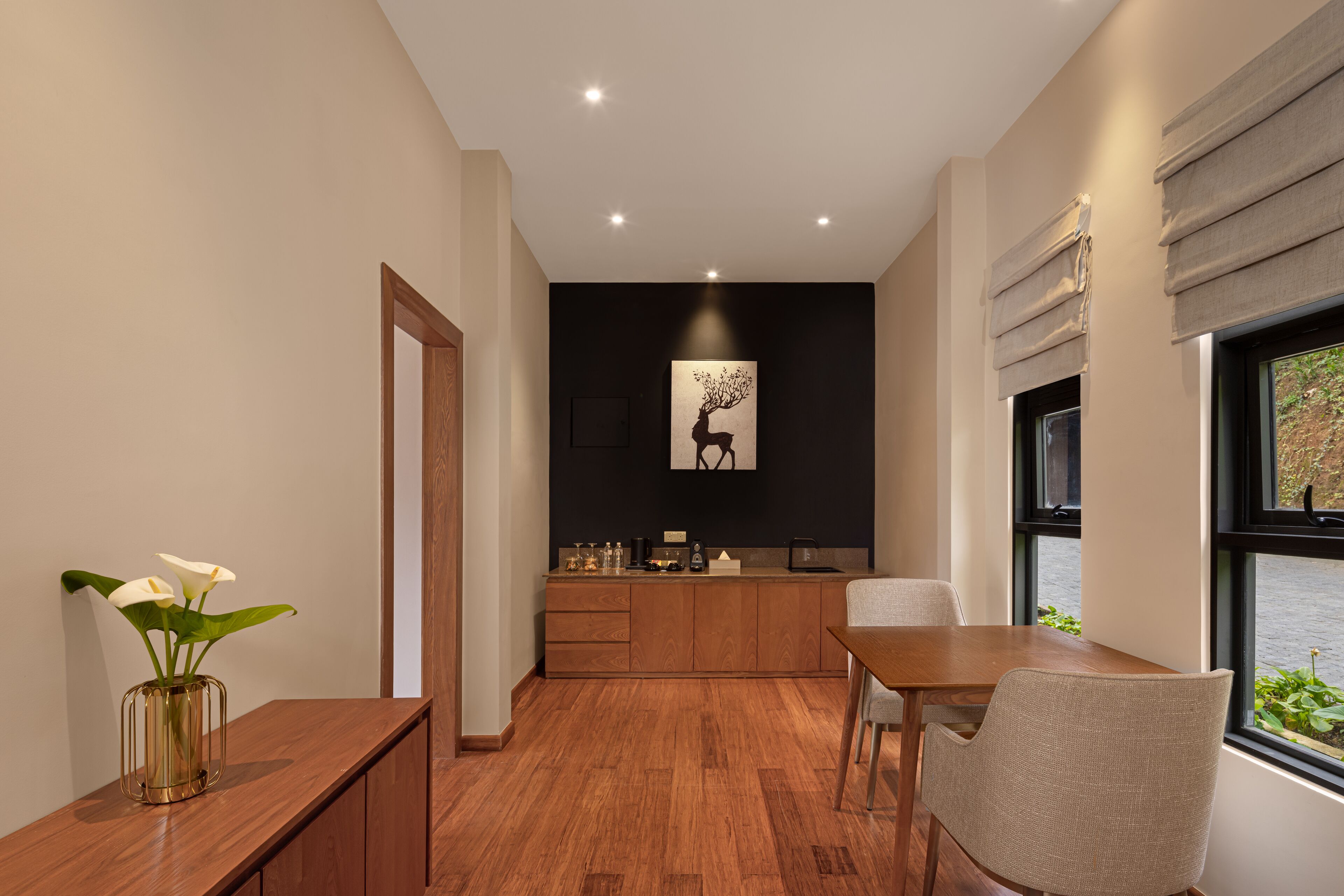 Una cocina moderna con armarios de madera, una mesa de comedor y sillas. Hay un jarrón con flores blancas sobre una consola de madera.