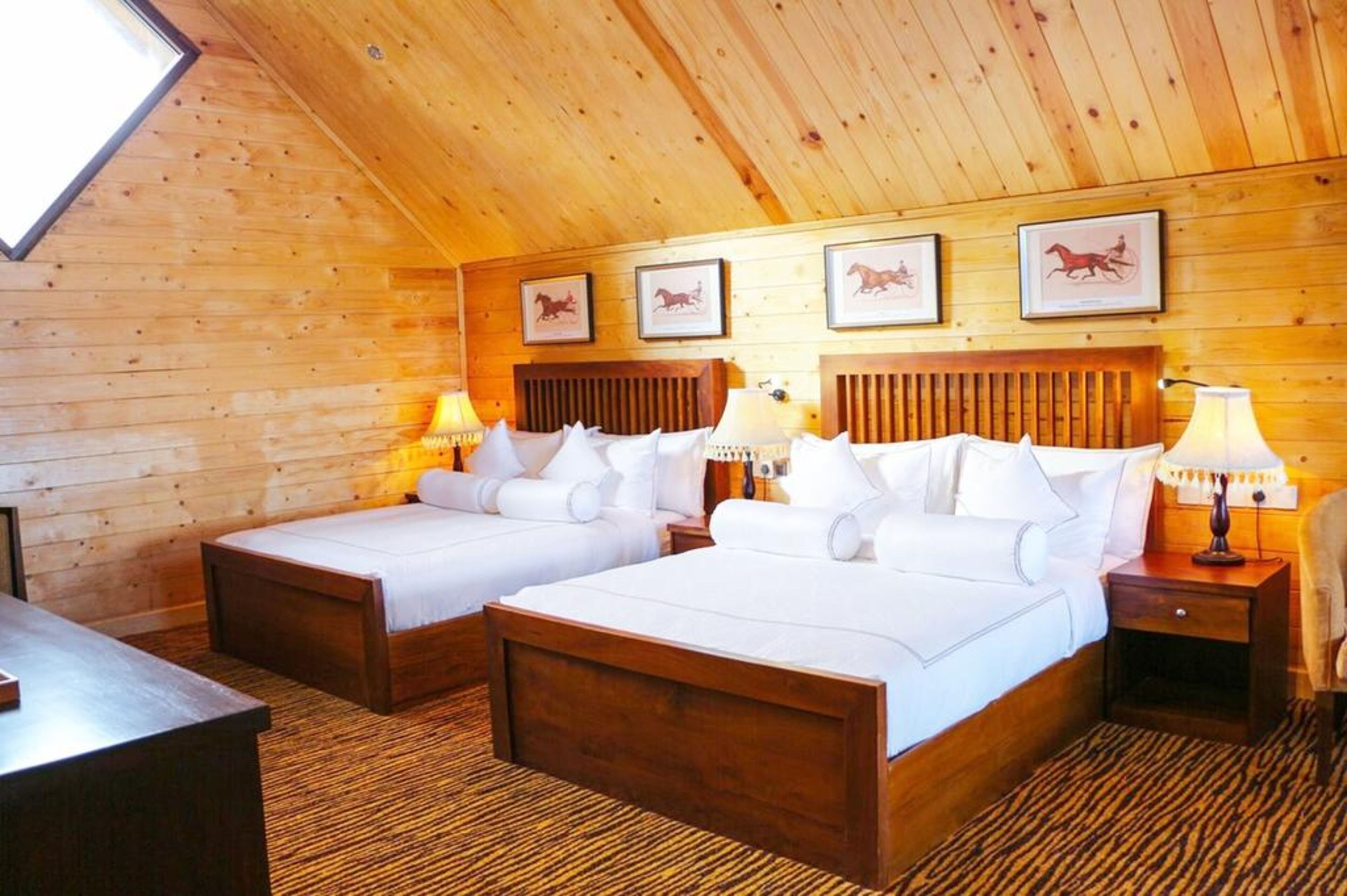 A room with two beds, wooden walls, and framed pictures on the wall.