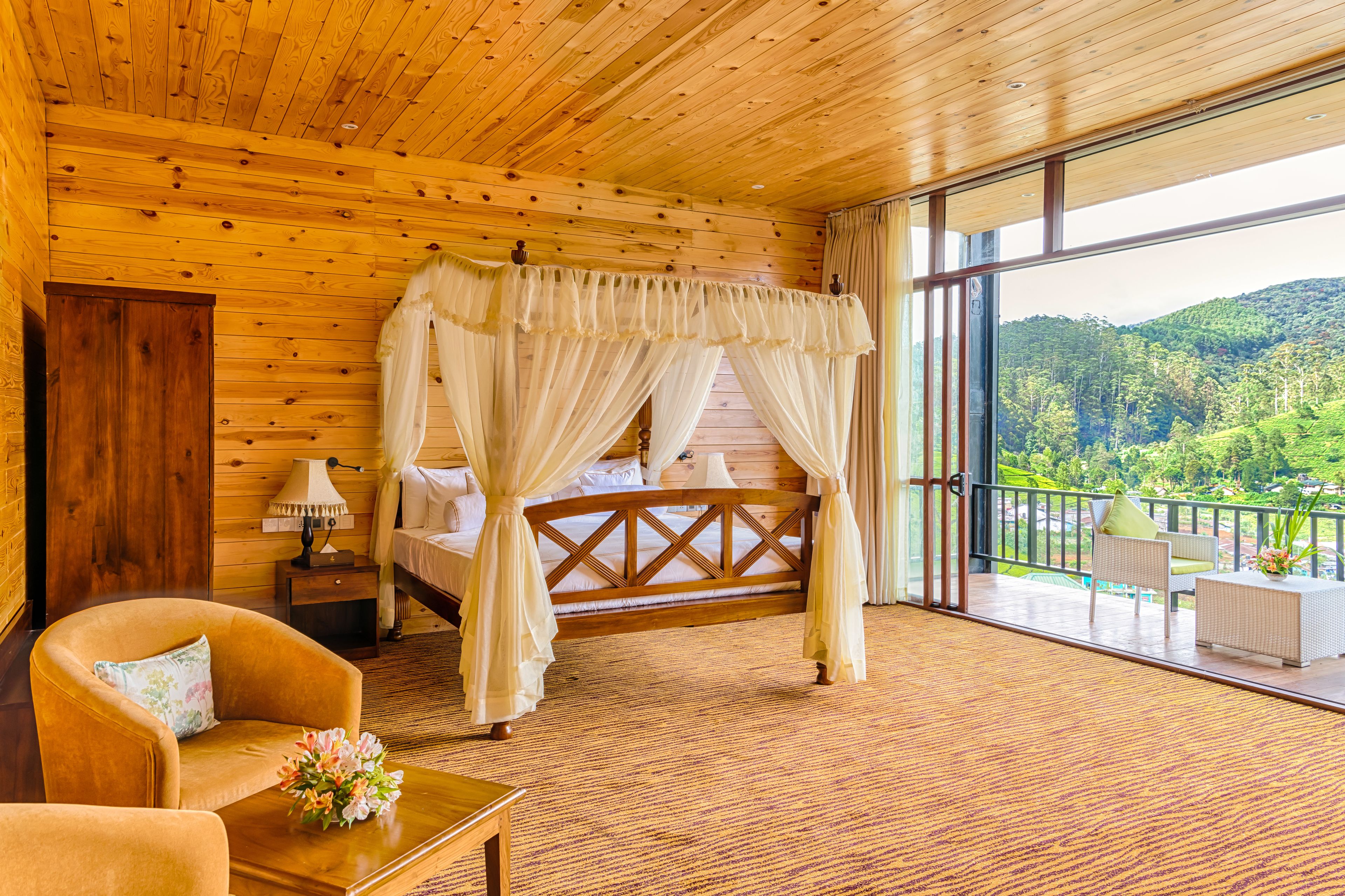 A wooden cabin room with a four-poster bed, a chair, a nightstand, and a view of the outdoors.