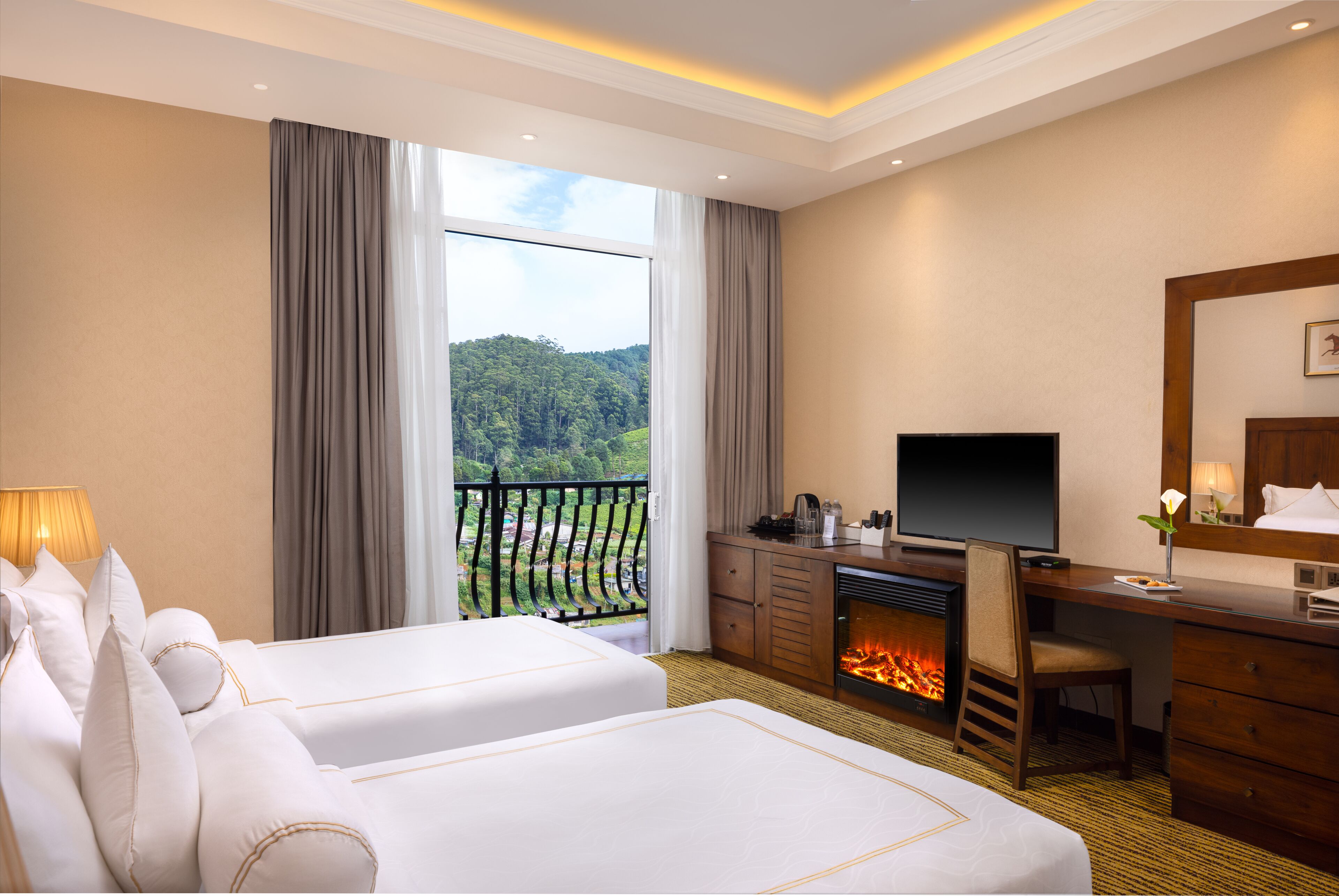 Habitación de hotel con dos camas, un escritorio con televisión, chimenea y balcón con vistas a la vegetación.