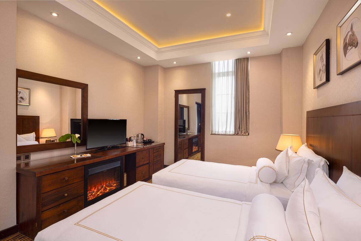 A hotel room with two beds, a television, a desk with a computer, and a fireplace.
