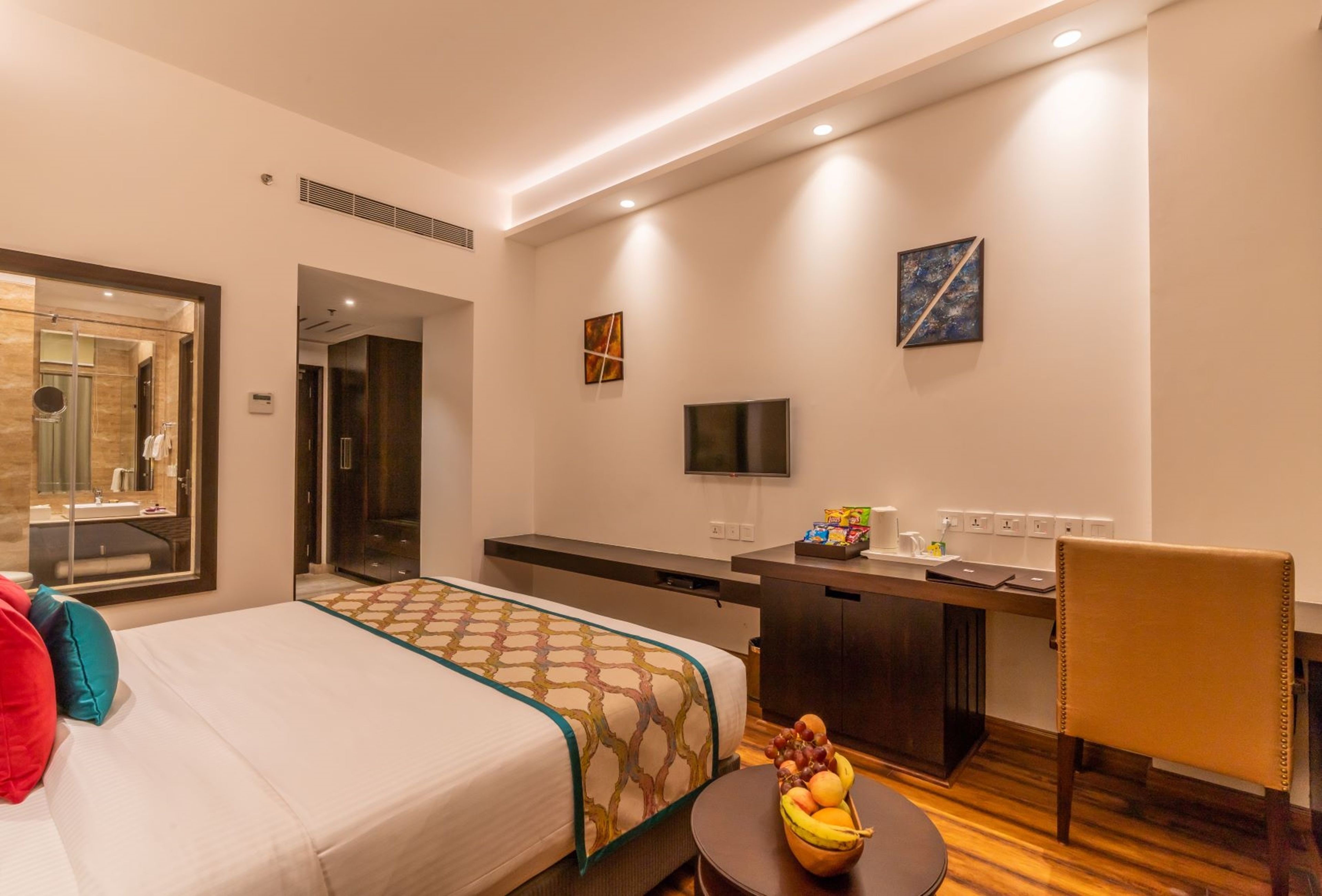 Habitación de hotel con una cama, un escritorio, una silla, un televisor y un frutero.