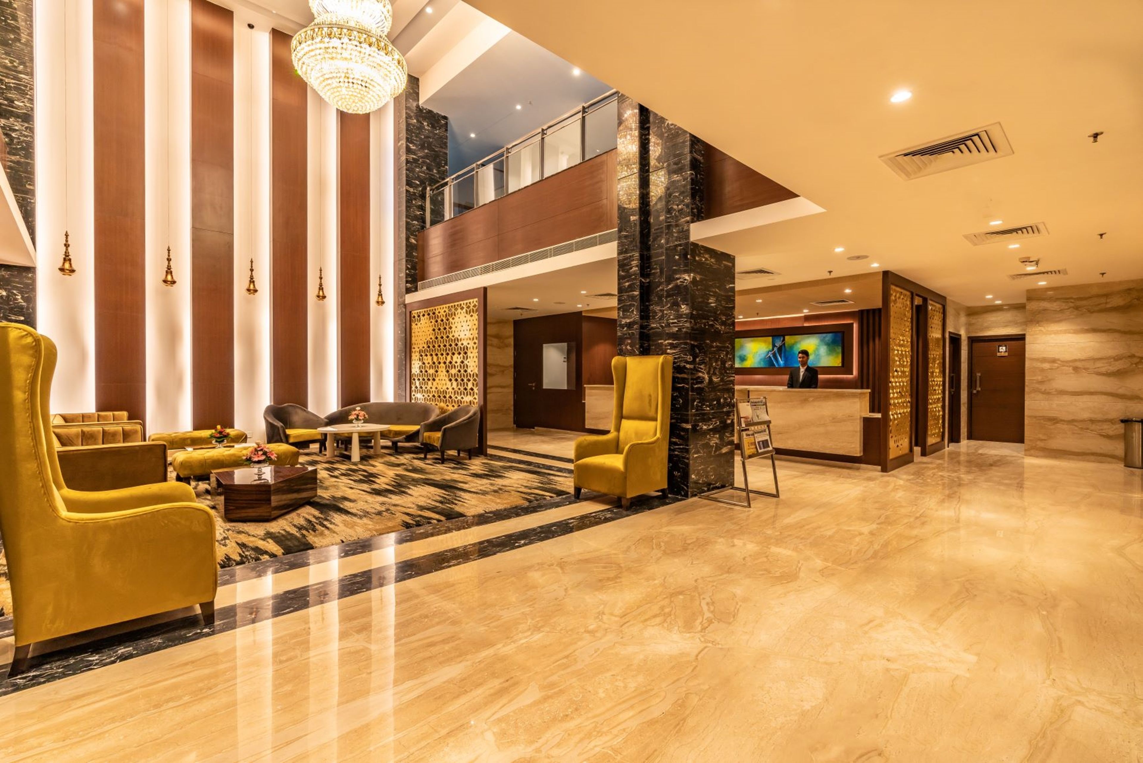 A spacious lobby with a high ceiling, a reception desk, and a seating area with yellow armchairs.