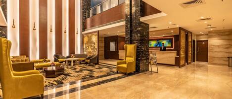 A spacious lobby with a high ceiling, a reception desk, and a seating area with yellow armchairs.