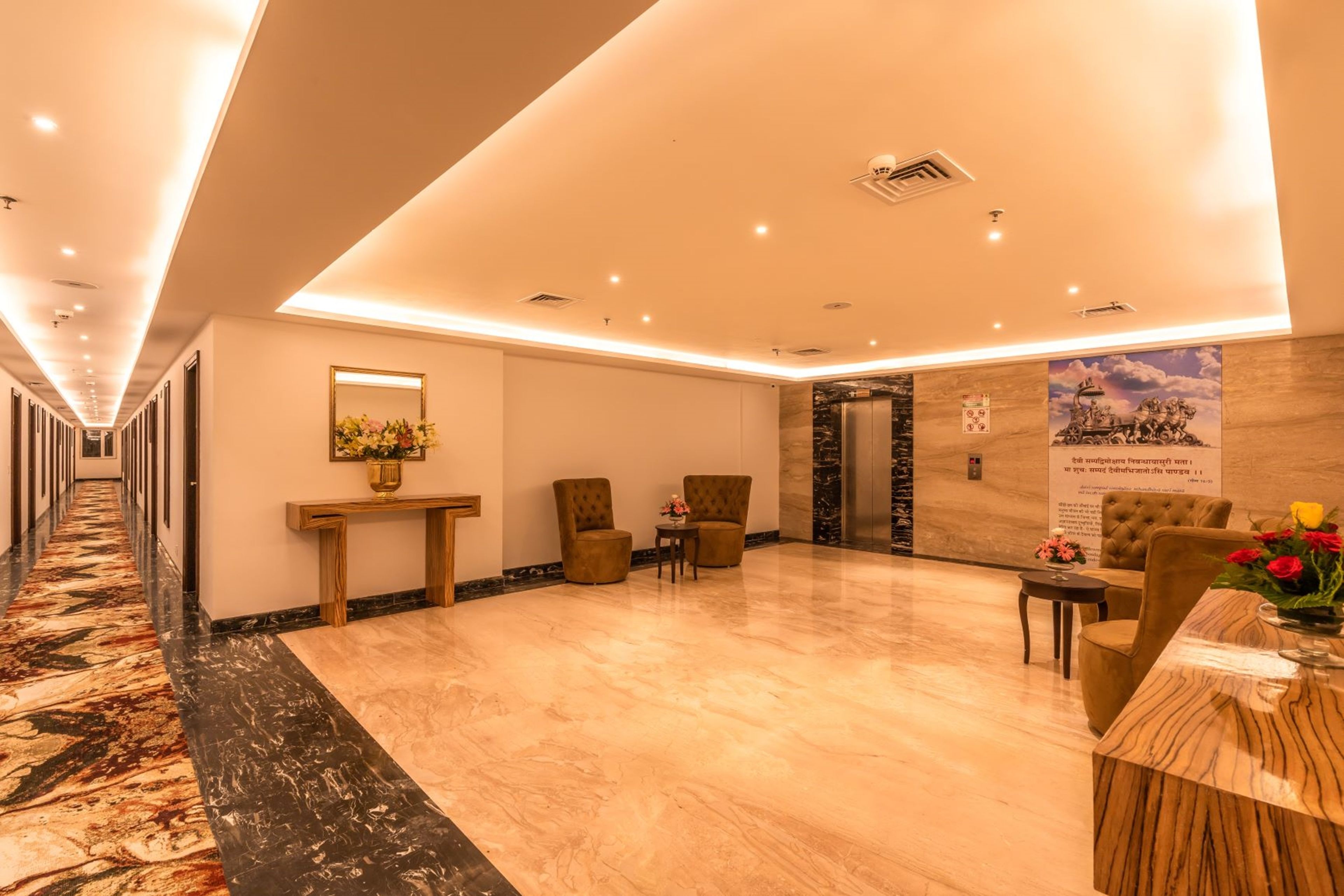 Vestíbulo de hotel con piso de mármol, mostrador de recepción, dos sillones, una mesita con flores y un letrero en la pared.