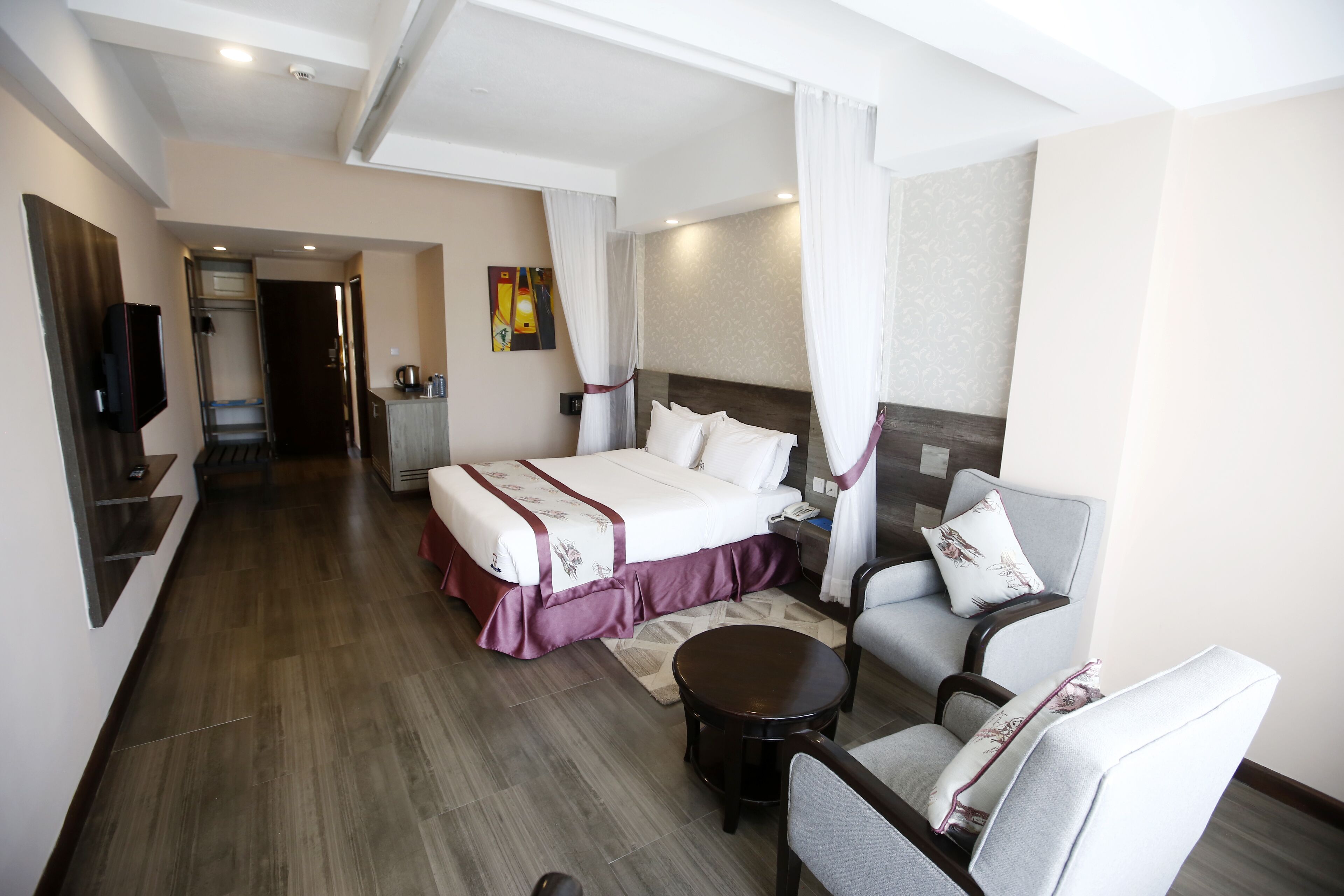 A hotel room with a bed, a sitting area with a chair and a small table, a television, and a bathroom visible through an open door.